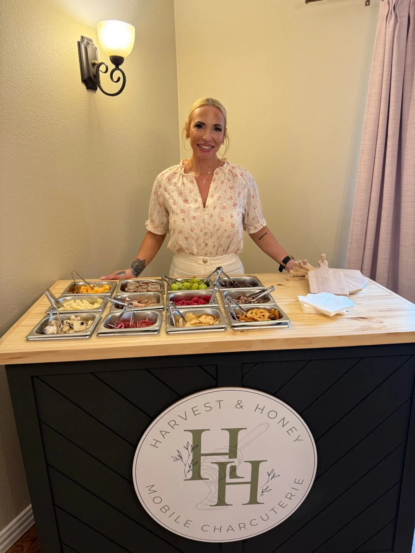 Jess smiling behind a charcuterie cart stocked with cheeses, fruit, meats, and crackers