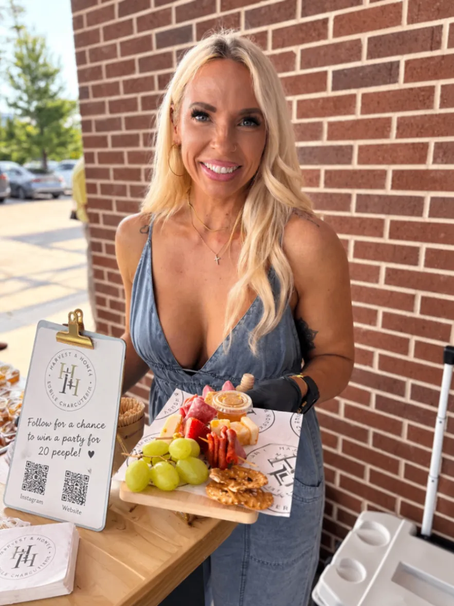 Jess, founder and owner of Harvest and Honey, smiling while holding a charcuterie board at an event